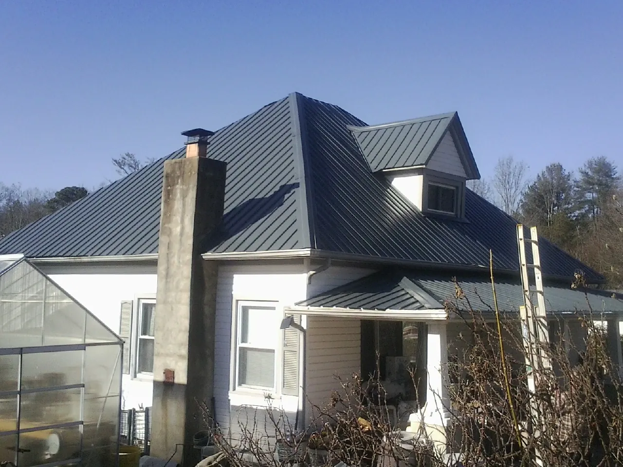 Dark blue standing seam metal roof on a white farmhouse with dormer — Slate & Tile Roof Repair by Roofing Brothers in Fletcher