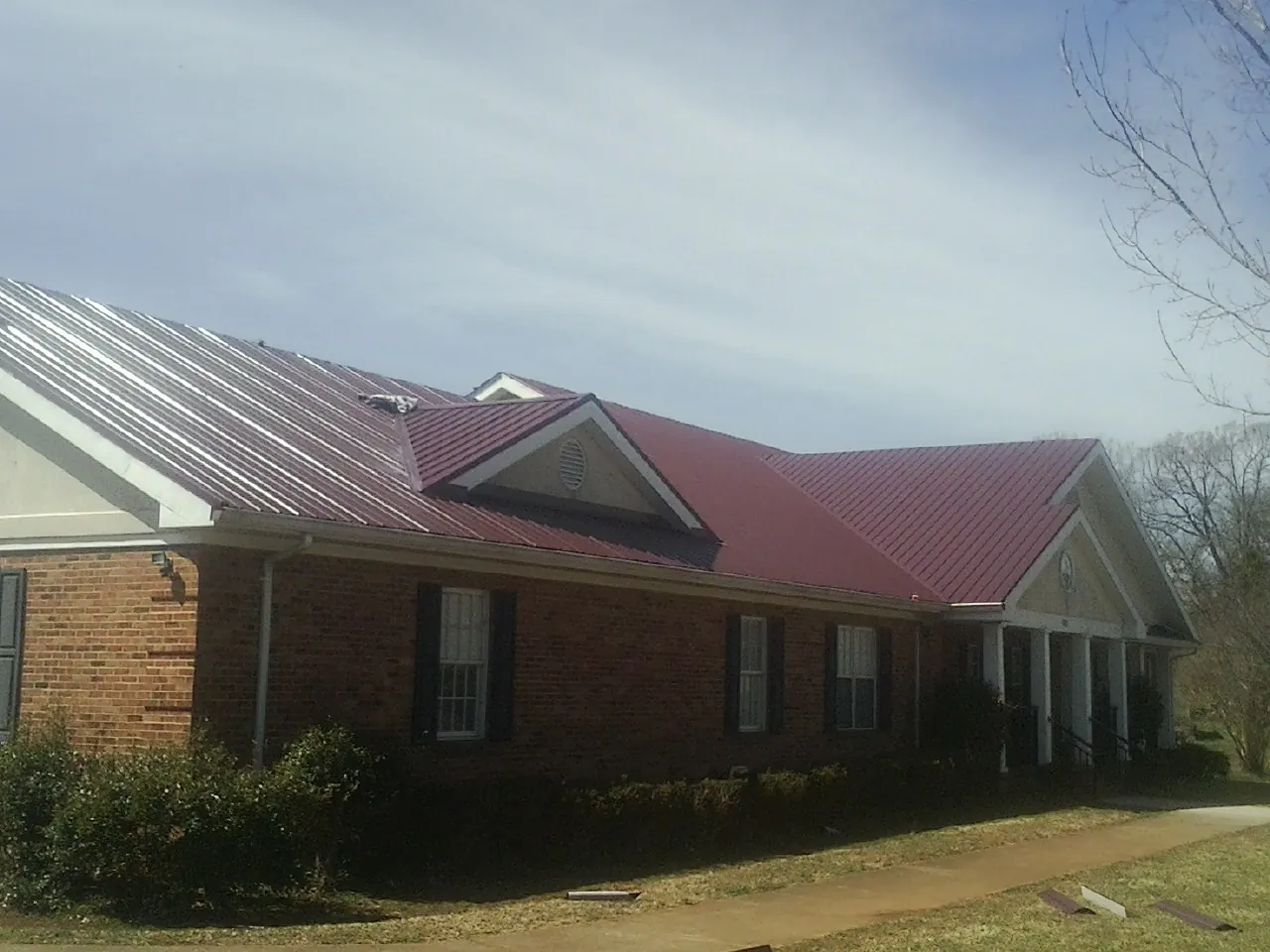 Red metal roof with gabled entries on a long brick building, from a Hail Damage Roof Repair job in Fletcher