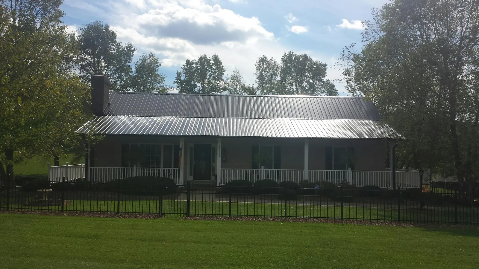Gray metal roof on a brick ranch with a full width front porch — Gutter Guard Installation work by our crew in Fletcher