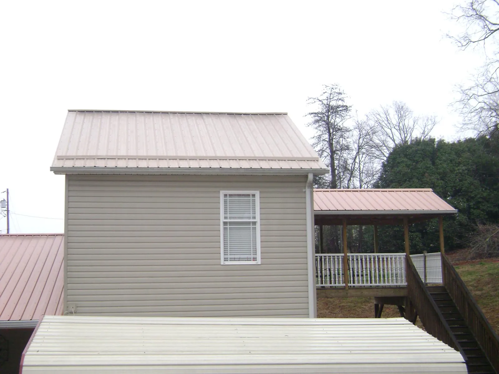 Tan metal roofs on a two story addition and attached porch, from a Roof Replacement job in Fletcher
